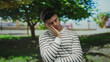 © Krakenimages.com - Young man in striped shirt with eyes closed appearing thoughtful in a serene park setting outdoors with greenery and trees in the background suggesting relaxation or daydreaming