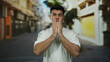 © Krakenimages.com - Young man stands on a city street looking concerned with hands on face, wearing a casual white shirt under daylight in an urban outdoor setting.