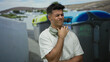 © Krakenimages.com - Young man with headphones poses on a city street expressing frustration near recycling bins surrounded by urban scenery and white architecture enhancing the outdoor atmosphere.