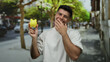 © Krakenimages.com - Young man smiling holding yellow piggy bank on busy city street with greenery around, capturing a joyful outdoor moment showcasing savings and urban lifestyle.