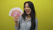 © Krakenimages.com - Young chinese woman holding yuan banknotes over isolated yellow background, embodying celebration and success.