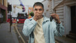 © Krakenimages.com - Man young hispanic holding car keys, one hand covering his face and eye while standing on an urban street with a bus and shopfronts visible; regret loss.