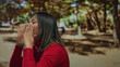 © Krakenimages.com - Young chinese woman shouting in an outdoor park wearing a red sweater, expressing excitement and confidence amidst lush greenery with trees in the background.