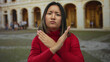 © Krakenimages.com - Young chinese woman making an x gesture with crossed arms in an outdoor university setting, wearing a red sweater, expressing dissatisfaction at an old architectural background.