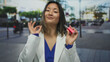 © Krakenimages.com - Woman in white blazer holding ecigarette on urban street in city outdoors, gesturing ok symbol with fingers, indicating approval or satisfaction, during daylight.