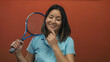 © Krakenimages.com - Young chinese woman with tennis racket poses against isolated red background wall, smiling and thoughtful.