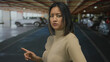 © Krakenimages.com - Woman pointing in an indoor parking area, surrounded by parked cars, exudes confidence with an assertive gesture suggesting direction or instruction.