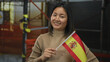 © Krakenimages.com - Woman smiling while holding spanish flag at construction site with scaffolding in the background, symbolizing international collaboration and cultural diversity outdoors.