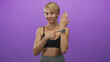© Krakenimages.com - Woman pointing at smartwatch on raised wrist wearing sports bra in studio with purple backdrop and fitness pose; confidence wellness vitality.