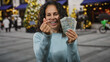 © Krakenimages.com - Middle-aged woman in peru making heart gesture with fingers while holding peruvian soles outdoors in urban city street.