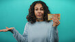© Krakenimages.com - Middle-aged woman holding south african banknote with indecisive gesture against blue background.