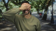 © Krakenimages.com - Young hispanic man covering eyes playfully while standing outdoors in a lively urban street surrounded by trees on a sunny day, creating a joyful, relaxed atmosphere.