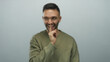© Krakenimages.com - Young man in casual sweatshirt making shushing gesture with finger on lips against plain white background, expressing silence or secrecy with a playful smile.