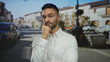 © Krakenimages.com - Young hispanic man looking thoughtful and tired on an urban street, wearing a white shirt, captured in a city setting with cars and buildings in the background.