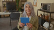 © Krakenimages.com - Senior woman with grey hair holding tablet in modern office setting, surrounded by contemporary furniture and decor, expressing concentration during her workday.