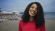 © Krakenimages.com - Woman smiles revealing teeth and face framed by curly hair on a sunlit sandy beach by the sea; summer joy.
