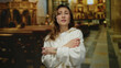 © Krakenimages.com - Young woman in a church interior appears fearful clutching arms with a worried expression symbolizing anxiety and emotion surrounded by religious motifs creating a dramatic atmosphere.