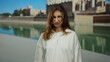 © Krakenimages.com - Young woman frowning outdoors in mallorca near cathedral on sunny day, wearing white sweater, reflecting mood against city backdrop with clear sky and serene water