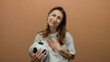 © Krakenimages.com - Woman smiling softly holding soccer ball against brown background, exhibiting contentment and sports enthusiasm.