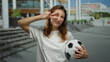 © Krakenimages.com - Young woman holding soccer ball gesturing peace sign outdoors in urban city street during daytime.