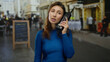 © Krakenimages.com - Young woman holding retro phone on city street, dressed in blue, conveying urban nostalgia amidst a lively outdoor backdrop with blurred pedestrians.