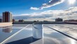 © Jackie - white paint can sits on a freshly coated flat rooftop under bright blue sky the surface is smooth and reflective showing clouds and sun buildings are visible in the distance