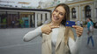 © Krakenimages.com - Woman in city holding credit card with thumbs up, expressing success and happiness, while standing outdoors in a lively urban street environment.
