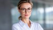 © buraratn - Confident businesswoman with glasses standing in a modern office setting, showcasing professionalism and determination in her expression, with a blurred background