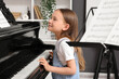 © Pixel-Shot - Cute little happy girl with notes playing grand piano at home