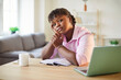 © Studio Romantic - Portrait of pensive female writer at table at home. Young African American woman sitting at work desk with open notebook, coffee mug and laptop, leaning cheek on hand, looking at camera and thinking