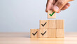 © Athiphat - Wooden blocks with check marks stacked in pyramid shape, hand placing top block with green check, symbolizing completed tasks, organization, and achievement