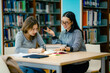 © Wanwajee - Female tutor helping student understand subject using books at library table education mentoring supportive learning atmosphere.