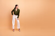 © deagreez - Woman in olive green blouse stands smiling against beige background wearing white wide leg pants a chic business portrait