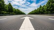 © Bayu Tri Nugroho - Wide empty highway with white arrow pointing straight ahead through lush green trees under blue sky with clouds for travel and road trip themes