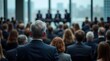 © Dedewijaya - Business professionals attending a conference or meeting with speakers on stage in the background, observed from behind the audience