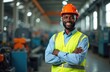 © Pete - Smiling Black engineer man in orange helmet and yellow vest stands with arms crossed in factory. Industrial worker near machines poses confidently indoors. Pro male employee at work.