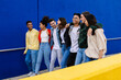 © Xavier Lorenzo - Group of cheerful young students walking together against a blue wall, enjoying their time together