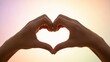 © Lakshmi - Hands forming a heart shape against a bright, colorful sky.