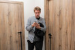 © Mihail - A man stands in a changing room looking at his phone while holding a black jacket