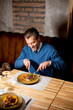© BGStock72 - Man enjoying a meal at a restaurant with a wooden table in the evening
