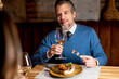© BGStock72 - Man enjoys meal and wine in restaurant while smiling at dining companion
