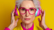 © Maryna - A stylish older woman in vibrant headphones and glasses exudes confidence against a bright yellow background.