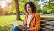 © Elenba - Young woman writing in a notebook while sitting on a bench in a park