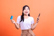 © Ajab - A happy young woman holds a credit card and smartphone, looking excited while shopping online, isolated on orange background