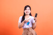 © Ajab - Young woman holding a credit card and a mobile phone, smiling and pointing at the card. She looks confident and ready to make a purchase isolated on orange background