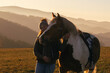© Annabell Gsödl - Woman gently holding her pinto horse outdoors in winter light, warm sunset mood and peaceful rural landscape