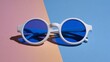 © thenort - Modern, round sunglasses with blue lenses lie on a two-toned pastel pink and blue surface, casting a shadow