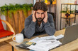 © Andrii Iemelianenko - Indian man at home leans on hands holds head sees unpaid bills on table by calculator and laptop. Arabian guy at desk checks dates counts costs plans payment low budget worried breathes slow and calm.