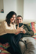 © Lomb - Happy mature couple making video call together lying in bed smiling at smartphone screen
