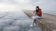 © Rendara Studio - Teenage girl using smartphone while sitting above the clouds on a concrete edge